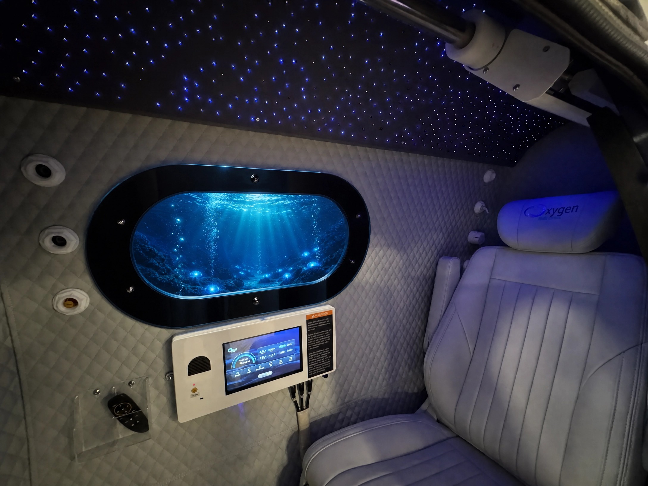 Interior of the XLS34D-Mini with the starlight fiber-optic ceiling glowing above the quilted walls, the oval window showing an underwater ocean scene, the touchscreen control panel, and the premium reclining seat
